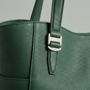 Macro view of deep green pebbled leather and brushed silver utility buckle detail.