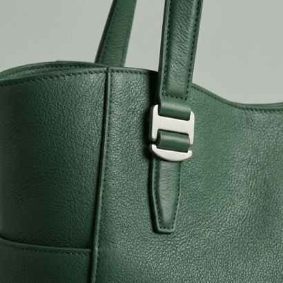 Macro view of deep green pebbled leather and brushed silver utility buckle detail.