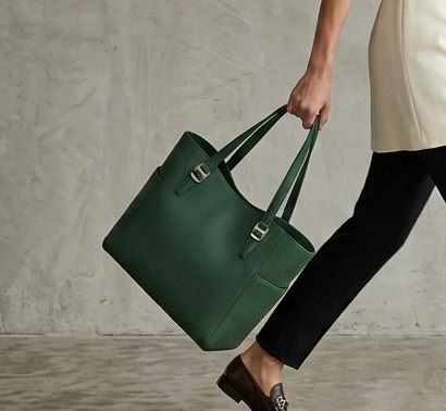 Woman carrying a deep green architectural leather tote walking in a minimalist studio.